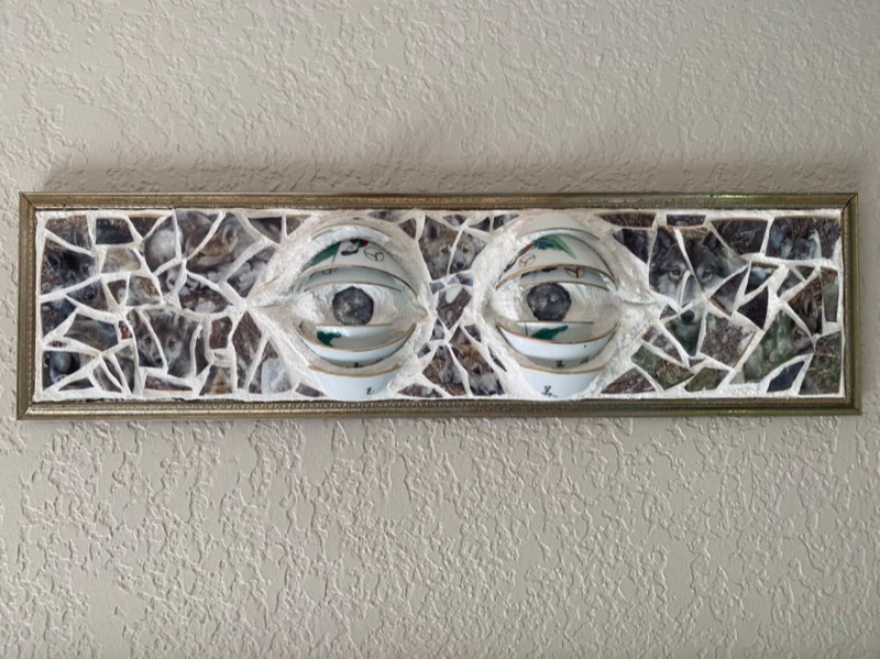 Window to the Wolf — two eyes formed from white china set into a long mosaic of wolf imagery in a gold frame